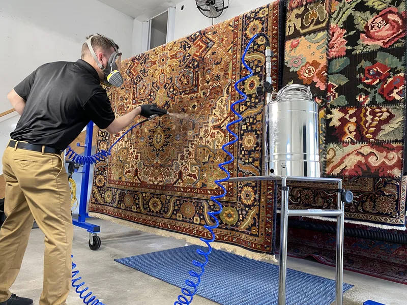 A technician spraying Fiber ProTector onto a rug hung on the rack at the Fiber Specialties Boise facility
