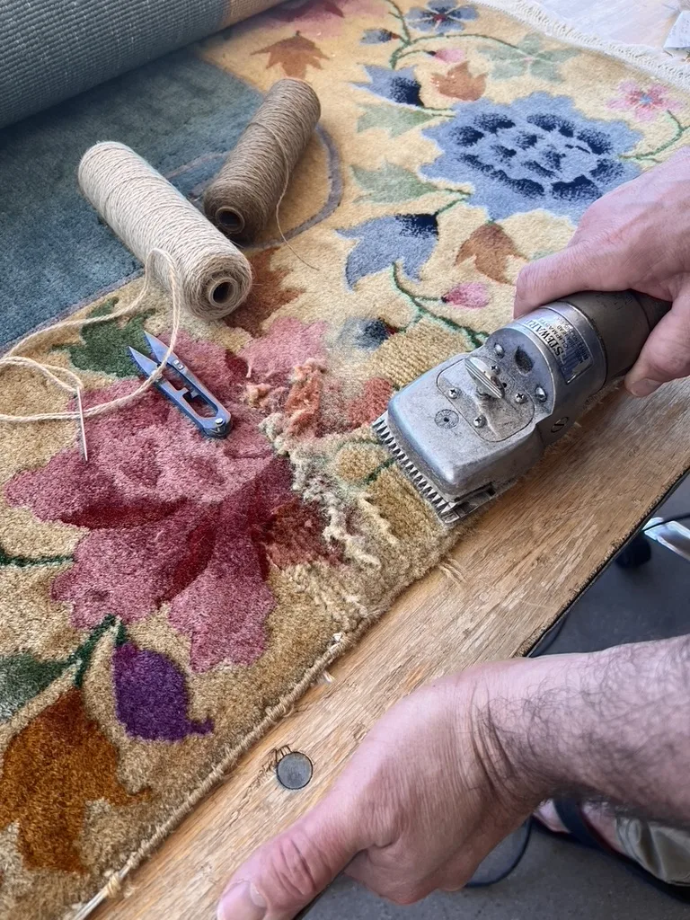 Worn pile being rebuilt on a floral hooked rug at the Fiber Specialties repair bench in Boise