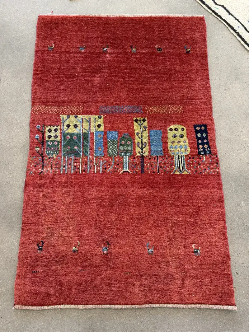 A red Lori Gabbeh rug with small pictorial figures at the Fiber Specialties Boise shop