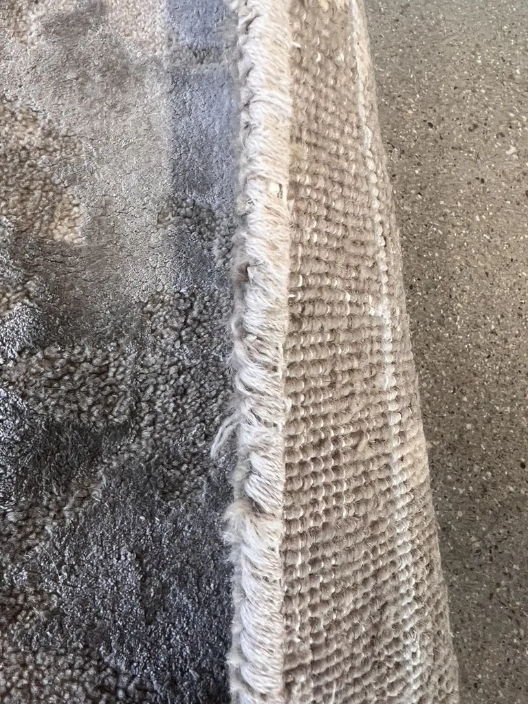 The edge of a wool rug eaten thin by moth larvae, photographed during inspection in Boise