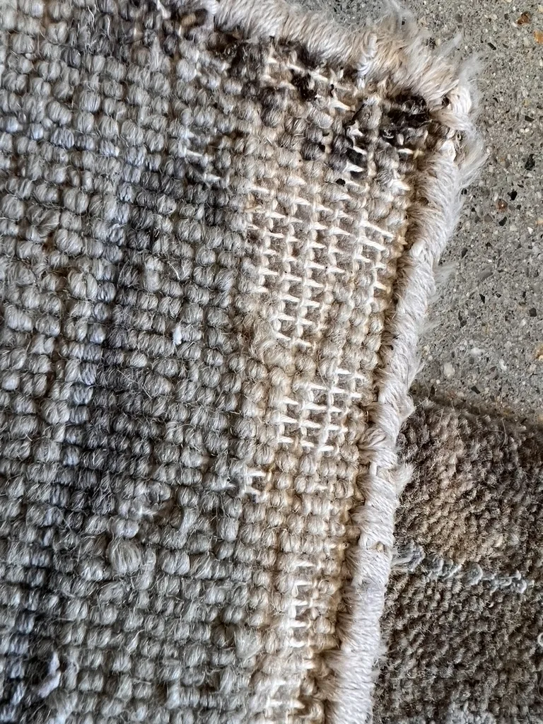 The back of a moth damaged rug showing the cotton foundation left behind where the wool pile was eaten