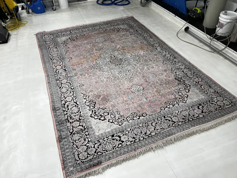 A fine hand-knotted rug with a pink field and black border, washed at the Fiber Specialties Boise facility