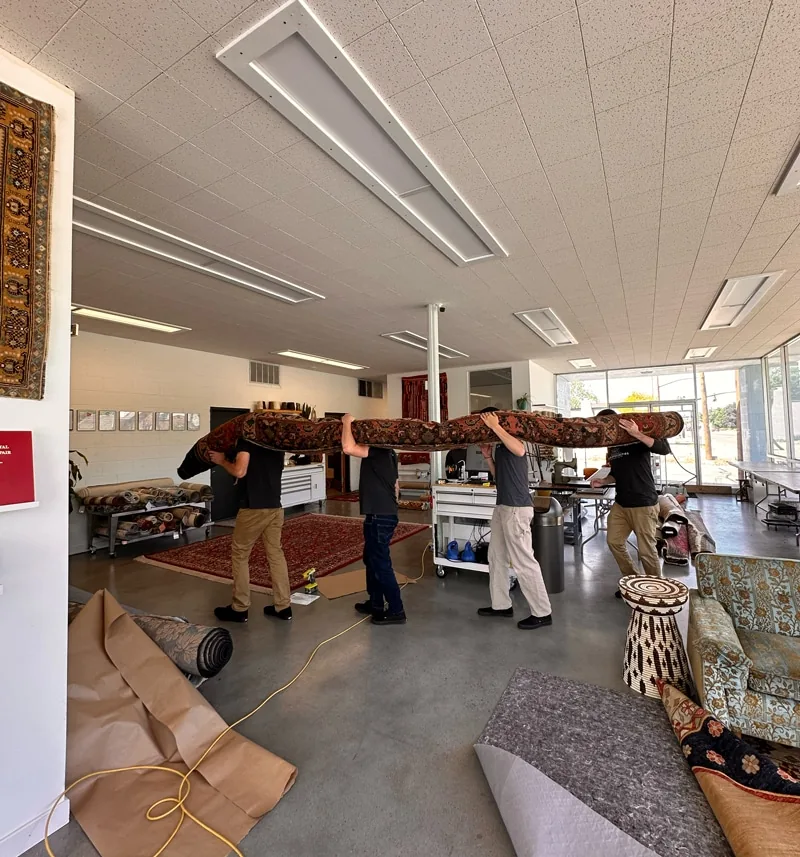 Four Fiber Specialties team members carrying a large rolled Persian rug through the Boise facility