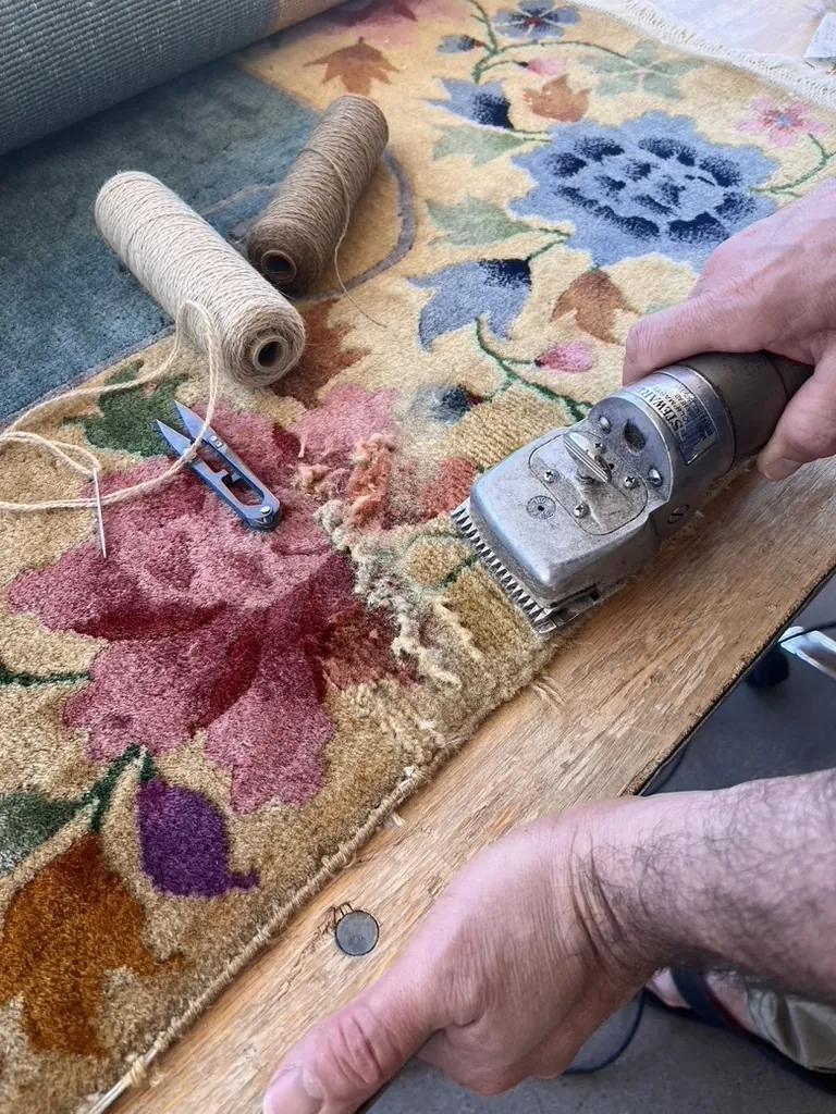 A technician levels a repaired area on a hand-knotted rug with electric shears at the Fiber Specialties Boise shop, repair thread and tools alongside