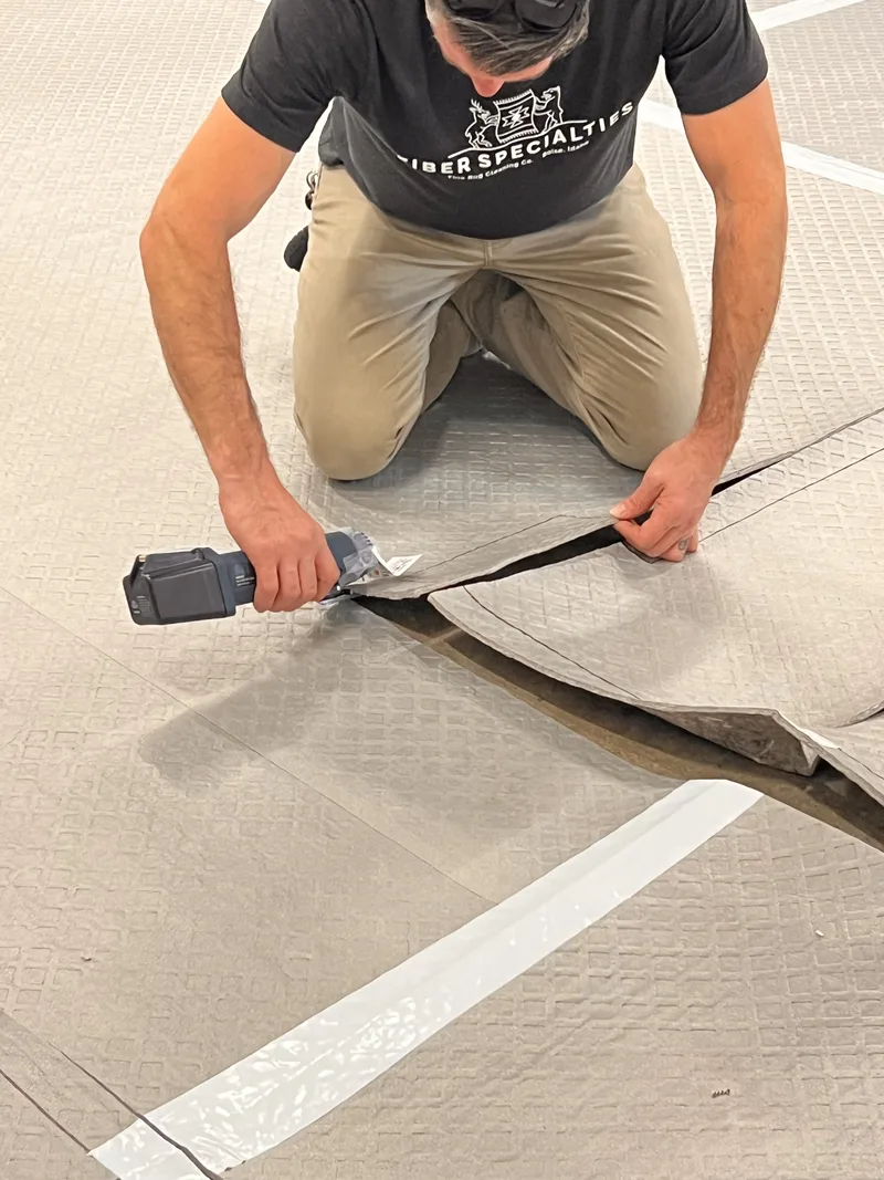 A technician cutting a custom rug pad to size on the floor of the Fiber Specialties Boise shop