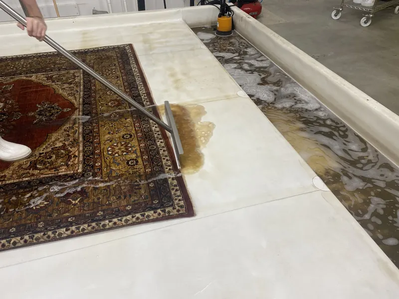 A technician squeegees dirty wash water out of a hand-knotted rug during a full-immersion wash at the Fiber Specialties Boise facility