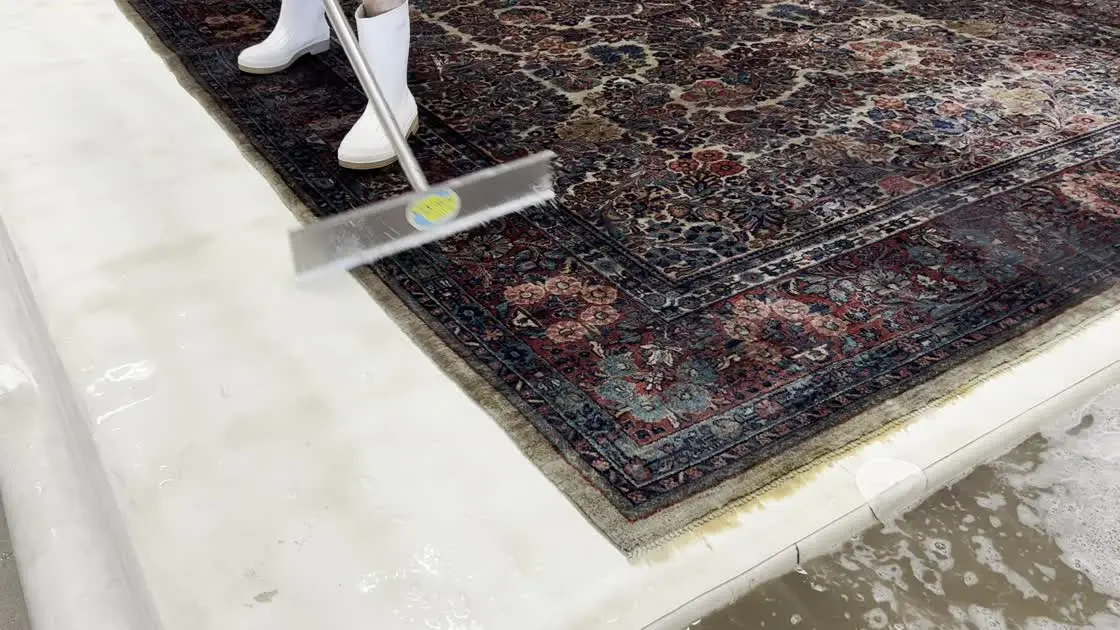 A technician squeegees wash water across a hand-knotted rug during a full-immersion wash on the Fiber Specialties Boise wash floor