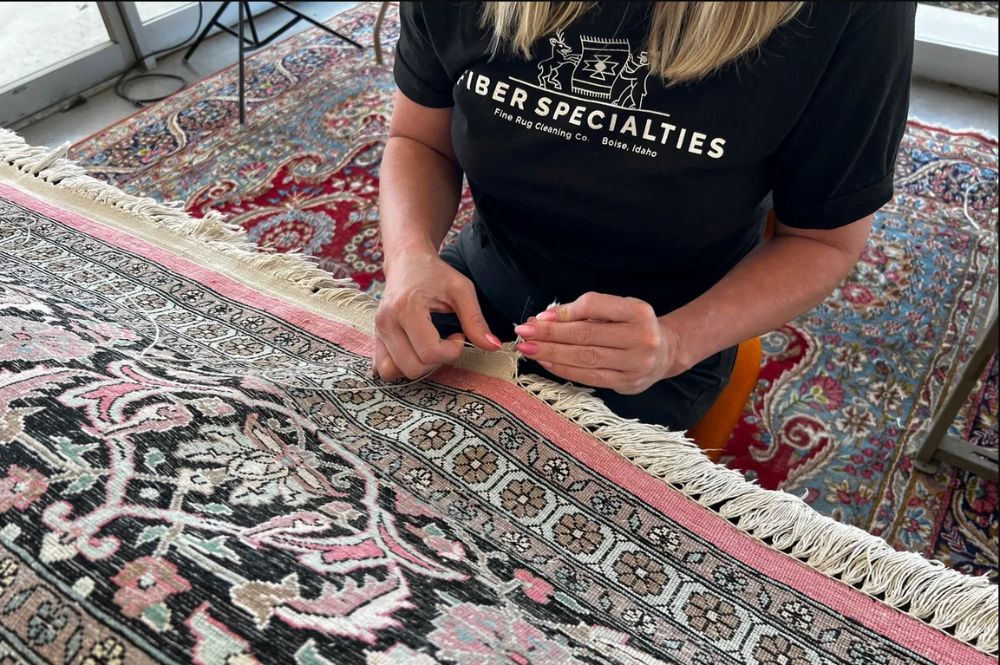 A woman hand sewing a rug fixing a small tear on the fringe.