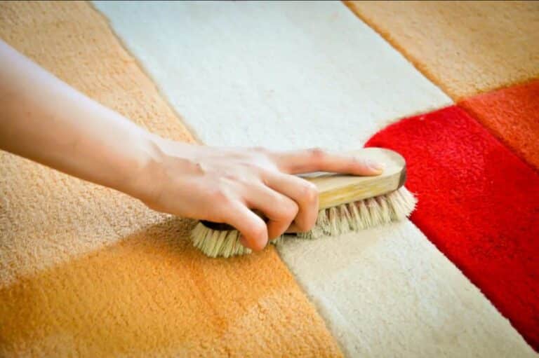 A person cleaning an area rug with a hand brush showing the before and after of carpet cleaning.