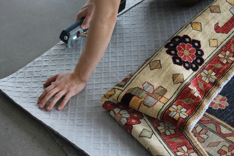 A custom felt rug pad being cut to size beside a hand-knotted rug at the Fiber Specialties facility in Boise
